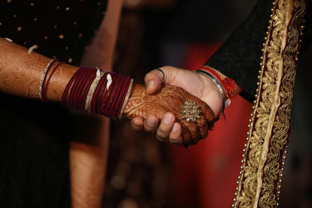 Close-up of a couple's hands with henna and bangles, symbolizing unity in an Indian wedding ceremony.